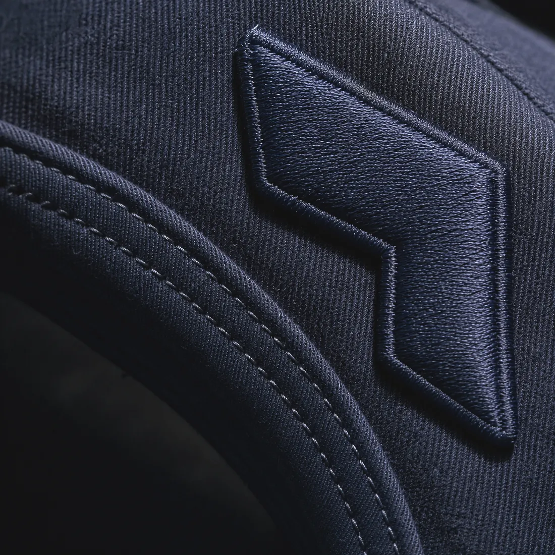 Macro detail of visor stitching rows and raised front-panel embroidery on a custom baseball cap
